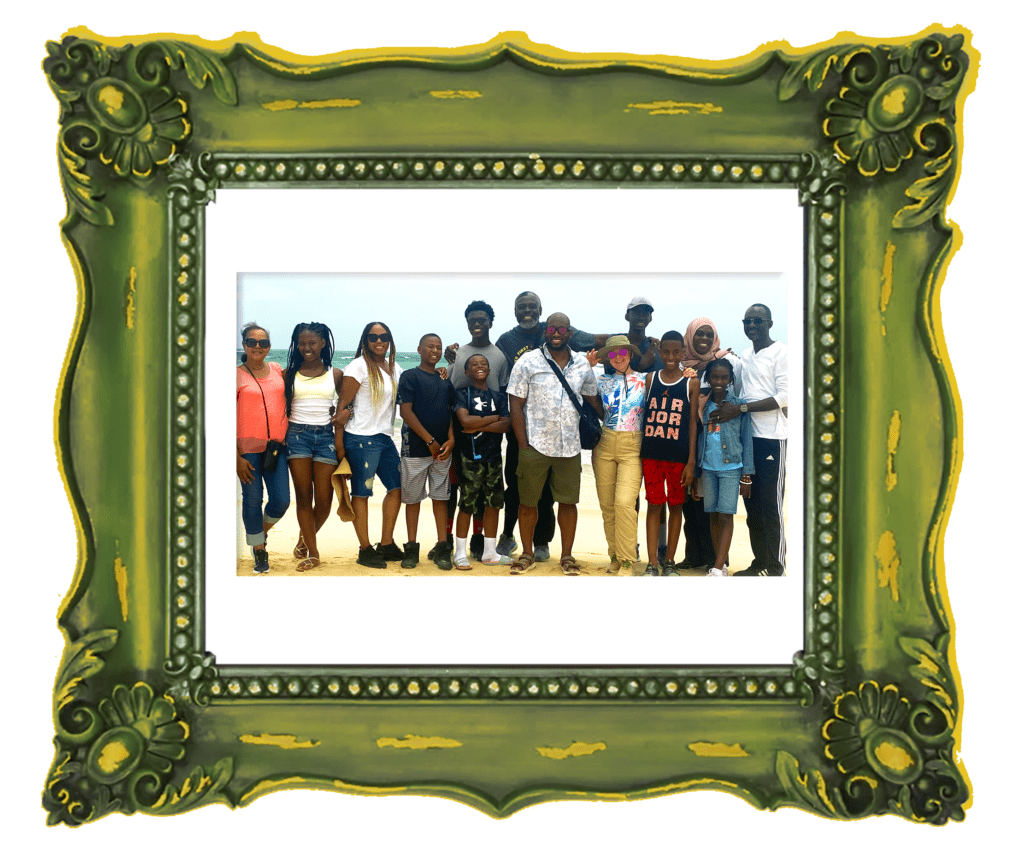 A photo of a large family standing smiling on the beach with the ocean behind them on a bright sunny day.